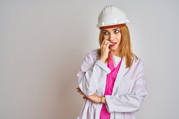 Redhead caucasian woman engineer wearing safety helmet over isolated background looking stressed and nervous with hands on mouth biting nails. Anxiety problem.