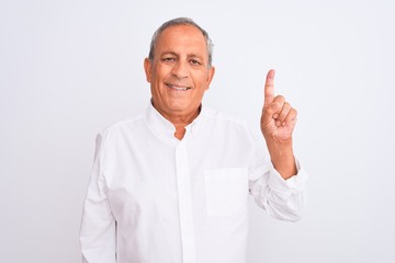 Senior grey-haired man wearing elegant shirt standing over isolated white background showing and pointing up with finger number one while smiling confident and happy.