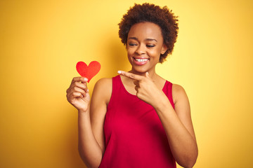 African american woman holding romantic paper hearts over yellow isolated background very happy pointing with hand and finger