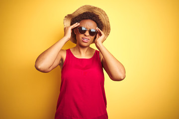 African american woman wearing summer hat and sunglasses over yellow isolated background suffering from headache desperate and stressed because pain and migraine. Hands on head.