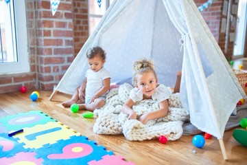 Beautiful toddlers playing inside tipi over blanket around lots of toys at kindergarten © Krakenimages.com