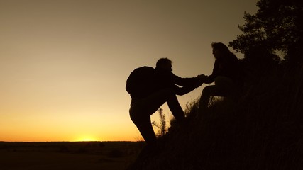 female traveler holds the hand of a male traveler helping to climb top of the hill. Tourists climb mountain at sunset, holding hands. team work of business partners. Happy family on vacation.