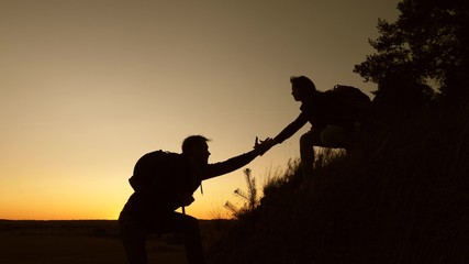 female traveler holds the hand of a male traveler helping to climb top of the hill. Tourists climb mountain at sunset, holding hands. team work of business partners. Happy family on vacation.
