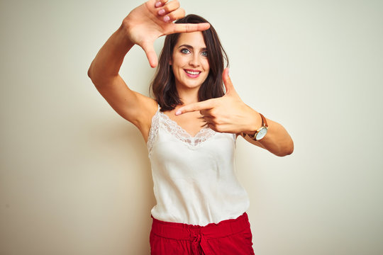 Young beautiful woman wearing t-shirt standing over white isolated background smiling making frame with hands and fingers with happy face. Creativity and photography concept.