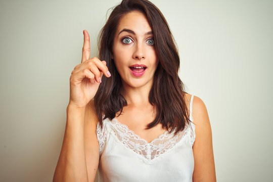 Young beautiful woman wearing t-shirt standing over white isolated background pointing finger up with successful idea. Exited and happy. Number one.