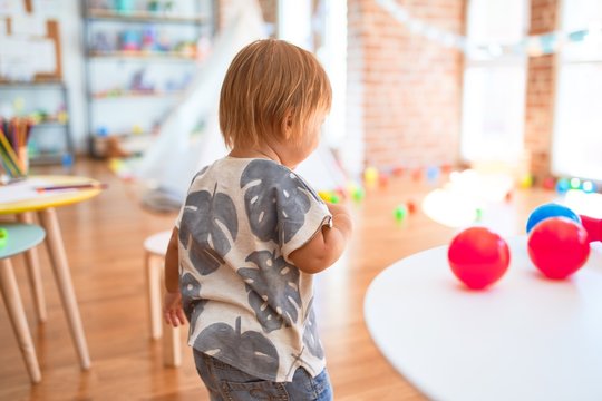 Adorable toddler playing with balls around lots of toys at kindergarten