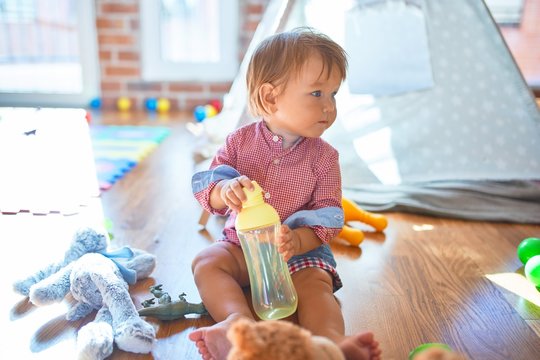 Adorable toddler holding feeding bottle around lots of toys at kindergarten