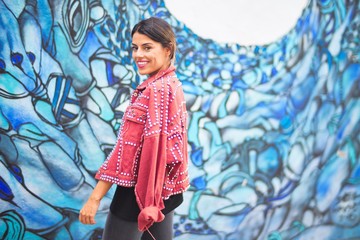 Young beautiful girl wearing red jacket standing backwards over colorful wall  at the town street