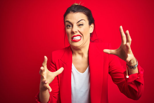 Young beautiful business woman standing over red isolated background Shouting frustrated with rage, hands trying to strangle, yelling mad