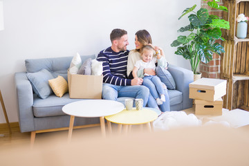 Beautiful family with kid sitting on the sofa drinking coffee at new home around cardboard boxes