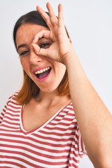 Beautiful redhead woman wearing casual striped red t-shirt over isolated background with happy face smiling doing ok sign with hand on eye looking through fingers