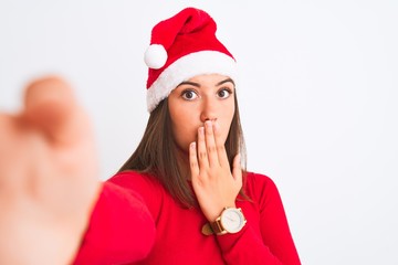 Girl wearing Christmas Santa hat make selfie by camera over isolated white background cover mouth with hand shocked with shame for mistake, expression of fear, scared in silence, secret concept