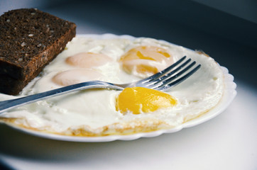 Fried eggs on a plate with brown bread, as the best and fastest breakfast in the morning for a cheerful day