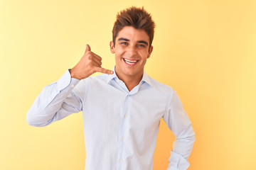 Young handsome businessman wearing elegant shirt over isolated yellow background smiling doing phone gesture with hand and fingers like talking on the telephone. Communicating concepts.