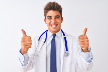Young handsome doctor man wearing stethoscope over isolated white background success sign doing positive gesture with hand, thumbs up smiling and happy. Cheerful expression and winner gesture.