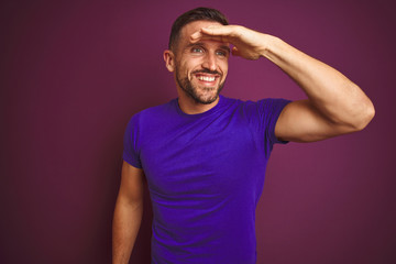 Fototapeta na wymiar Young man wearing casual purple t-shirt over lilac isolated background very happy and smiling looking far away with hand over head. Searching concept.