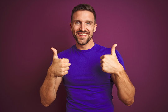 Young man wearing casual purple t-shirt over lilac isolated background success sign doing positive gesture with hand, thumbs up smiling and happy. Cheerful expression and winner gesture.