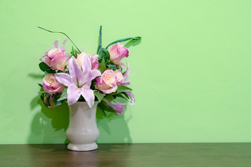 Pink lily and rose in vase on wooden table with green wall background