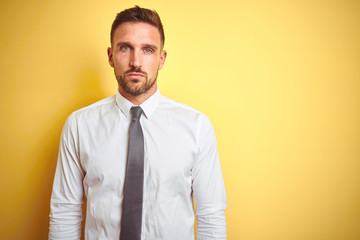 Young handsome business man wearing elegant white shirt over yellow isolated background Relaxed with serious expression on face. Simple and natural looking at the camera.
