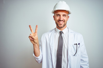 Young handsome engineer man wearing safety helmet over isolated background smiling with happy face winking at the camera doing victory sign. Number two.