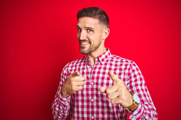 Young handsome man over red isolated background pointing fingers to camera with happy and funny face. Good energy and vibes.
