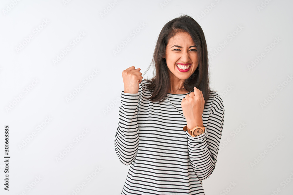 Wall mural Young beautiful chinese woman wearing striped t-shirt standing over isolated white background very happy and excited doing winner gesture with arms raised, smiling and screaming for success