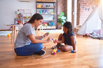 Beautiful teacher and toddler girl playing with train at kindergarten