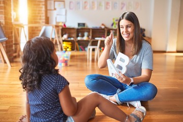 Beautiful teacher teaching alphabet to student toddler girl at kindergarten