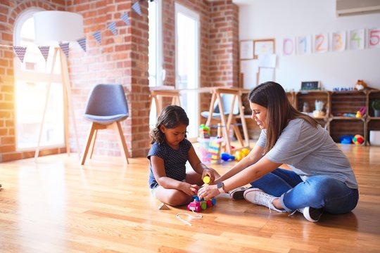 Beautiful teacher and toddler girl playing with train at kindergarten