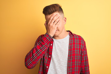 Young handsome man wearing casual shirt standing over isolated yellow background with sad expression covering face with hands while crying. Depression concept.