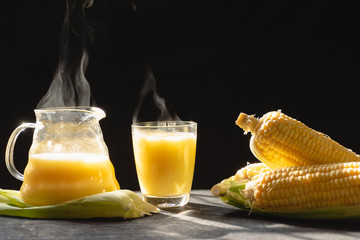 The steam from a jug and a glass of corn milk on black background, Warm drinks make good...