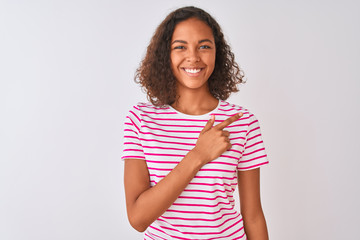 Young brazilian woman wearing pink striped t-shirt standing over isolated white background cheerful with a smile of face pointing with hand and finger up to the side with happy and natural expression