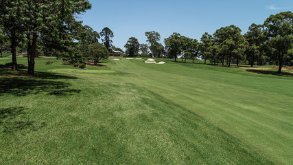 Golf course fairway, sand bunkers, lush green grass surrounded by trees against blue sky