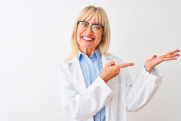 Middle age scientist woman wearing glasses standing over isolated white background amazed and smiling to the camera while presenting with hand and pointing with finger.