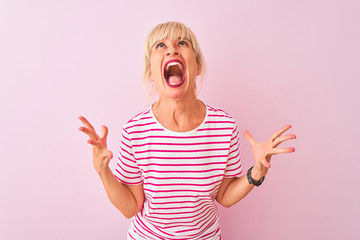 Middle age woman wearing striped t-shirt standing over isolated pink background crazy and mad...
