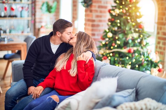 Young beautiful couple smiling happy and confident. Sitting on the sofa hugging and kissing around christmas tree at home