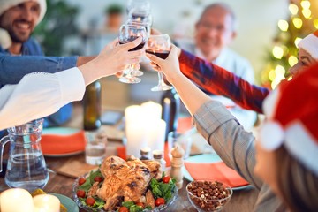 Beautiful family wearing santa claus hat meeting smiling happy and confident. Eating roasted turkey and toasting with cup of wine celebrating Christmas at home