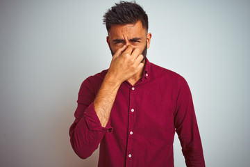 Young indian man wearing red elegant shirt standing over isolated grey background smelling...