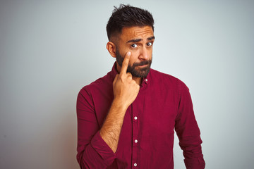 Young indian man wearing red elegant shirt standing over isolated grey background Pointing to the eye watching you gesture, suspicious expression