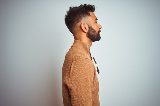 Indian man wearing elegant sweater and sunglasses standing over isolated white background looking to side, relax profile pose with natural face with confident smile.