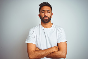Young indian man wearing t-shirt standing over isolated white background skeptic and nervous, disapproving expression on face with crossed arms. Negative person.