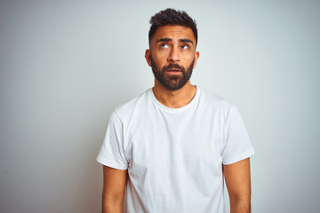 Young indian man wearing t-shirt standing over isolated white background looking sleepy and tired,...