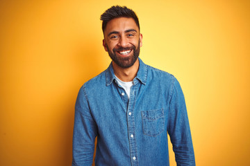 Young indian man wearing denim shirt standing over isolated yellow background with a happy and cool...