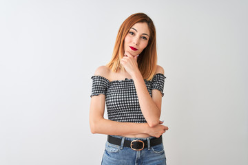 Beautiful redhead woman wearing casual t-shirt standing over isolated white background looking confident at the camera smiling with crossed arms and hand raised on chin. Thinking positive.