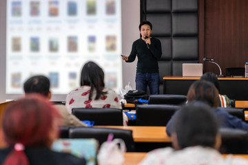 Asian Speaker or lecture with casual suit on the stage presenting via projector screen in the...
