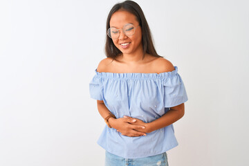 Young chinese woman wearing blue t-shirt and glasses over isolated white background with hand on stomach because indigestion, painful illness feeling unwell. Ache concept.