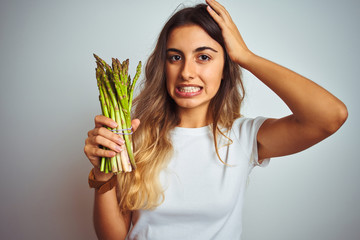 Young beautiful woman eating asparagus over grey isolated background stressed with hand on head, shocked with shame and surprise face, angry and frustrated. Fear and upset for mistake.
