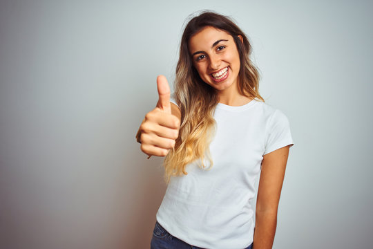 Young beautiful woman wearing casual white t-shirt over isolated background doing happy thumbs up gesture with hand. Approving expression looking at the camera showing success.