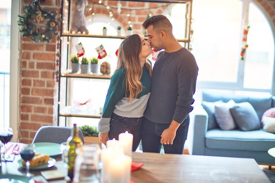 Young beautiful couple smiling happy and confident. Kissing and hugging around christmas decoration at home