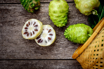 Close up Morinda citrifolia (Common name as Noni fruits, indian mulberry, cheese fruit) in basket with horizon sliced isolated on rustic wooden table background. Top view. Dark tone. Vintage style.